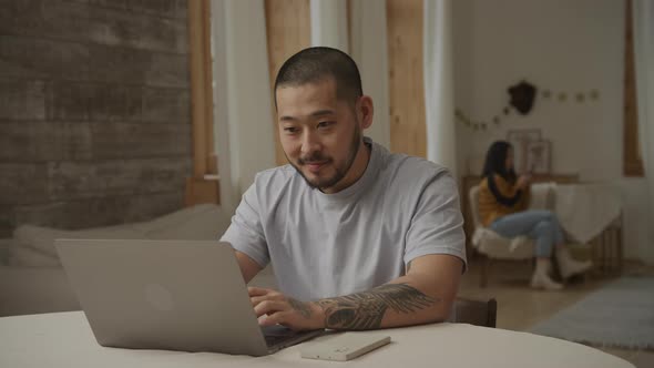 Happy Father Working Happy on His Laptop with His Wife Sitting in Background alt