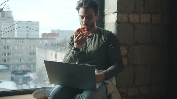 Arab Businessman Eating Pizza and Working with Laptop Computer Indoors in Loft Style Office alt