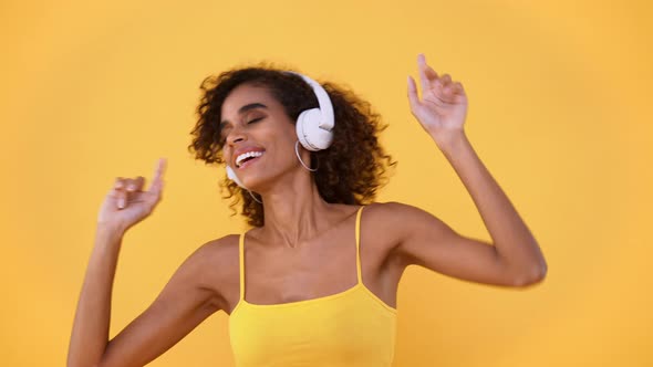 Happy African American woman listening to music on wireless headphones and dancing