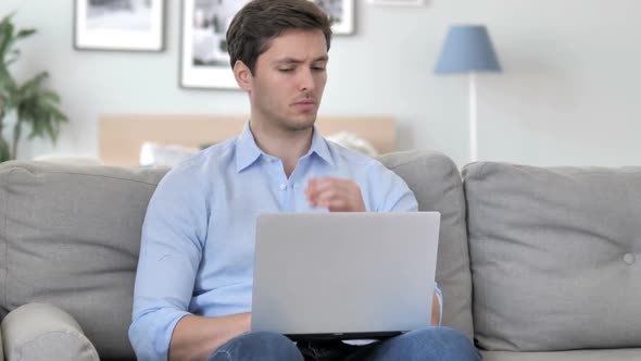 Handsome Young Man Thinking and Working on Laptop While Sitting on Couch alt