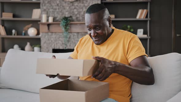 Happy Surprised African Senior Man Open Cardboard Box with Gift Unpacking Parcel Delivery Internet alt