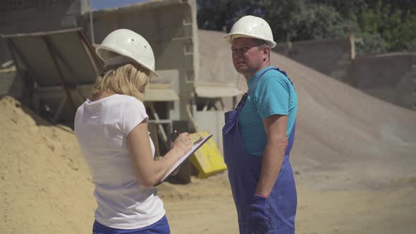 Middle Shot of Confident Caucasian Woman with Documents Talking To Adult Man Outdoors on Production alt