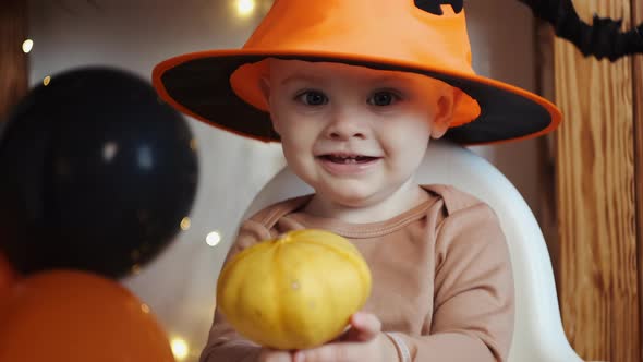 Portrait of Baby Boy Wearing Halloween Hat and Holding Little Pumpkin alt