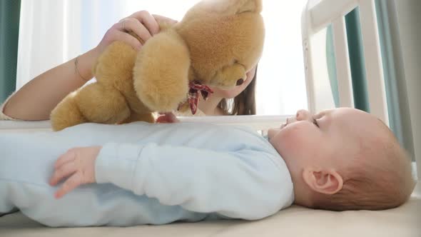Little Boy Looking and Reaching for Teddy Bear in His Cradle alt