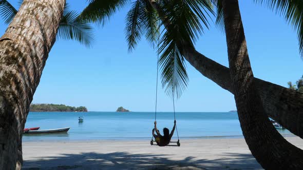 Man Swinging on a Paradisiacal Beach Under Palm Trees