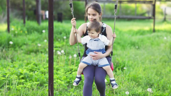 Cute Brother and Older Sister Ride on a Bright Swing on Warm Spring Day Against the Backdrop of a alt