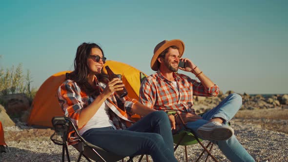 Happy Carefree Businessman with Wife or Girlfriend Relaxing with Beer in Camp Chairs Next to Tent on alt