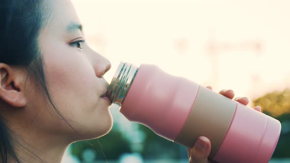 Asian young woman drinking water during workout. alt