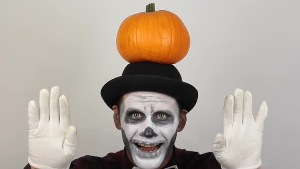 A Terrible Man in Clown Makeup and with a Pumpkin on His Head Grimaces and Waves His Hand in