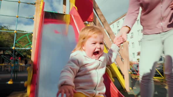 A happy little baby is rolling down a children's slide. alt