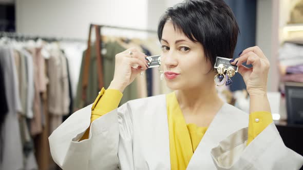 Portrait of Brunette Woman Trying on Earrings in Clothing Store Makes Grimaces and Smiling
