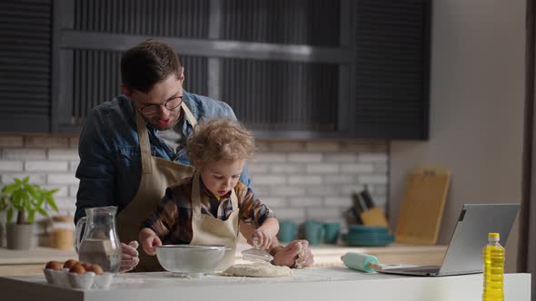 Man and His Baby Son are Cooking By Internet Recipe Man is Reading Info in Laptop and Toddler is alt