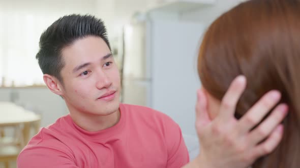Asian young loving couple sitting on sofa and looking at each other. alt