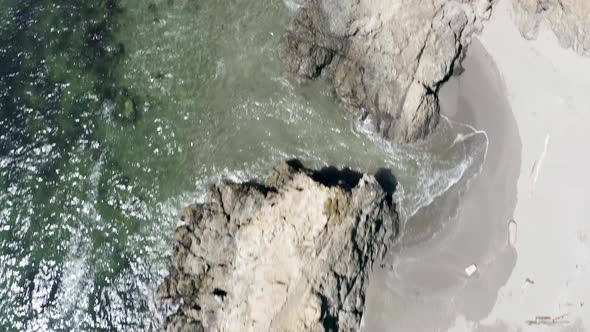 Aerial top-down view of crashing waves on a rocky beach alt