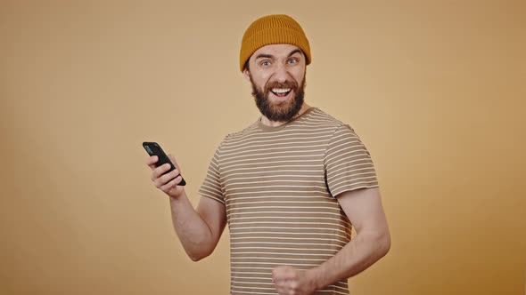 Mature Man Looks at Phone with Shocked Expression and Smiles alt