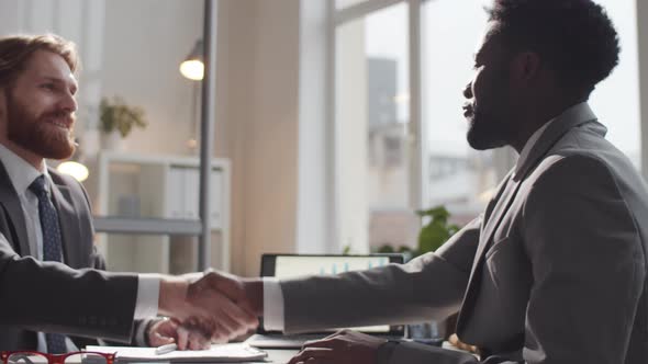 Two Young Multiethnic Business Associates Shaking Hands and Having Talk alt
