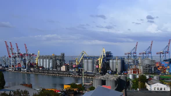 Port landscape with moving cargo loaders and grain elevators under blue sky