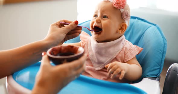 Portrait of Happy Young Baby in High Chair Being Fed By Mum