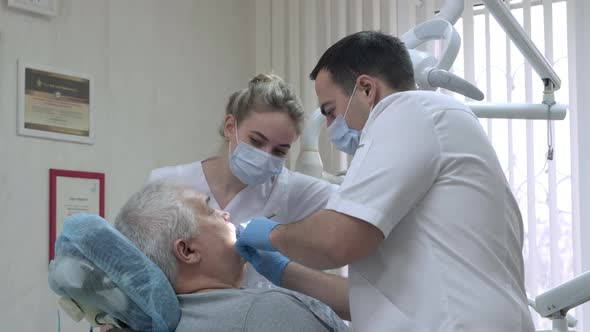 Dentist with Nurse in Protective Masks Working with Patient in Dental Clinic alt
