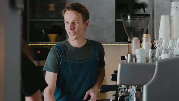 Smiling barista in a coffee shop making cappuccino coffee take away for a customer alt