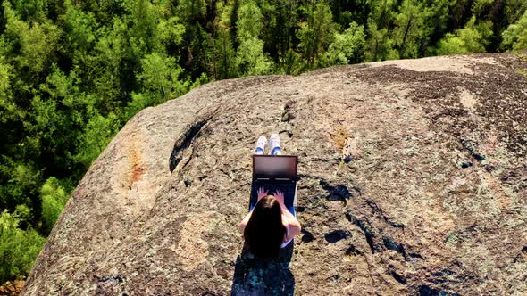 Top View of a Freelance Woman Typing on a Laptop at the Top of a Mountain