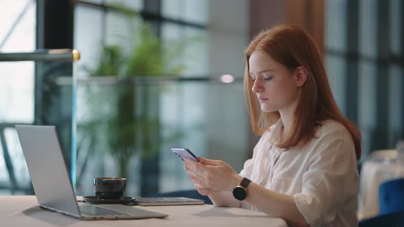 Female Office Worker in Coworking Place Sitting at Table with Laptop Using Cell Phone for Sending alt