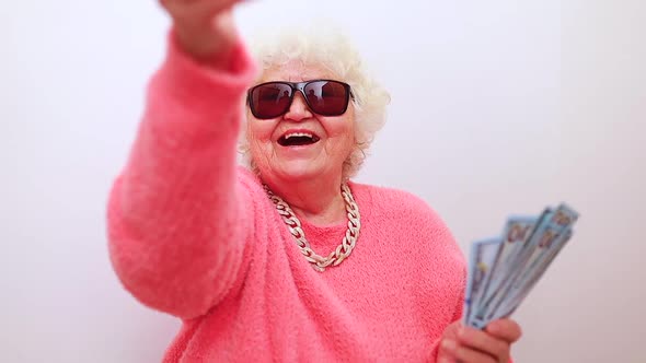 Blonde Old Lady Wear Pink Sweater and Sunglasses Showing Money Isolated White Background alt