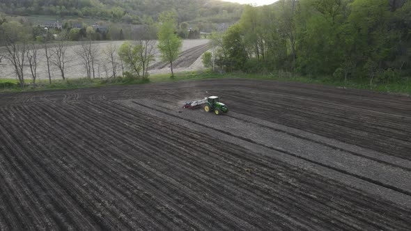 Farmer finish tilling field on a bright sunny day. Dust clouds following tractor. Forest on the hill