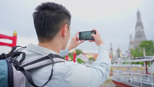 Asian man backpacker using mobile phone take picture of Buddha temple. alt