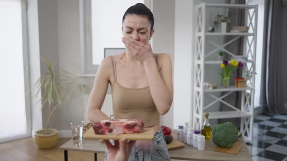 Portrait of Young Beautiful Vegan Woman Standing Indoors As Hand Showing Raw Meat alt