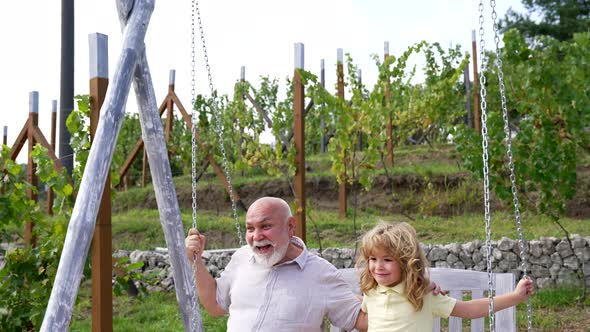 Happy Family of Grandkid and Grandfather Laugh Swinging Together in Backyard Fun