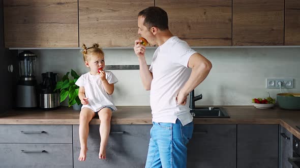 Cute Little Girl and Her Handsome Dad are Eating Fruit in Modern Kitchen alt