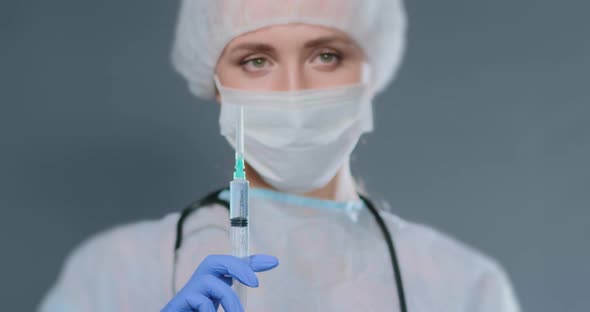 Young Woman in Coat Cap and Mask Holds Syringe Releasing Air alt