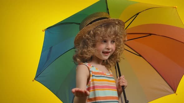 Cute Curly Blond Girl with a Rainbow Umbrella is Checking for the Rain alt
