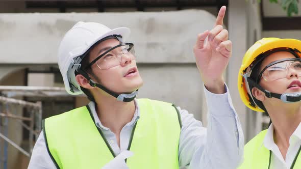Asian builder workers people wearing safety helmet, holding drawing working on construction side. alt