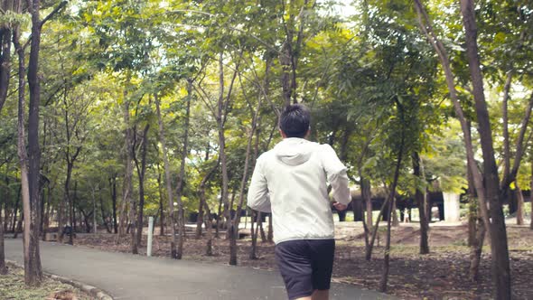 Young Asian man athlete running in a public park and enjoying beautiful forests.