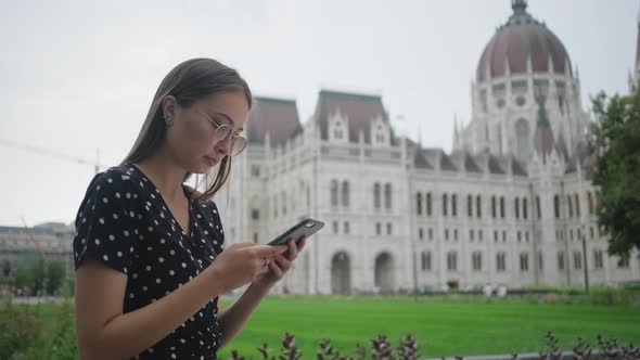 Young Woman is Reading Message in Smartphone Outdoors alt