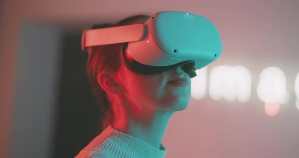 Young woman looking around moving head wearing vr goggles in neon lights alt