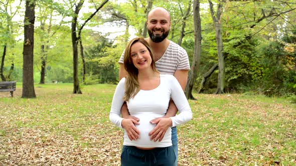Happy Couple - Handsome Man and Young Happy Pregnant Woman Holding Hands on Belly and Smile alt