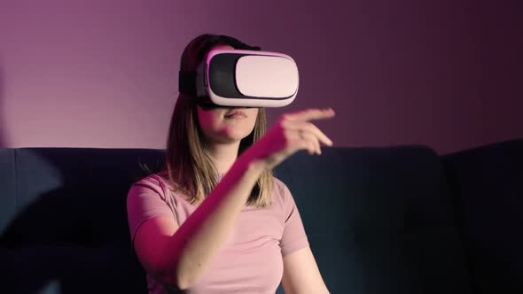 Woman Is Sitting on Sofa in Virtual Reality Glasses and Playing Video Game
