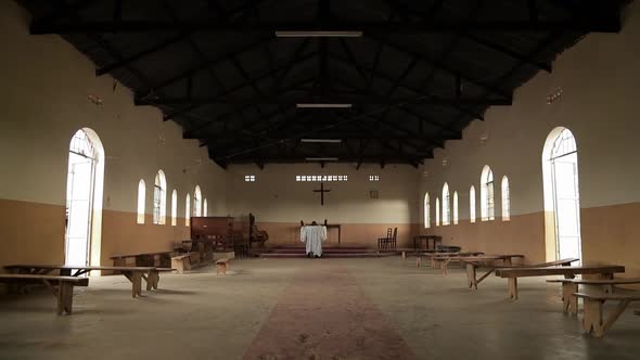 African Christian priest kneeling and praying in an empty church. alt