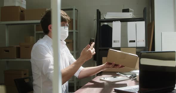 Man Employee of Warehouse Wearing Medical Mask Taking Delivery Box and Writing Information About alt