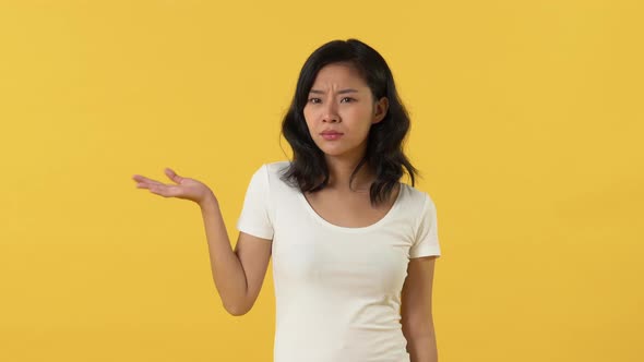 Asian girl expressing no and don't care gestures by shrugging shoulders with open hands