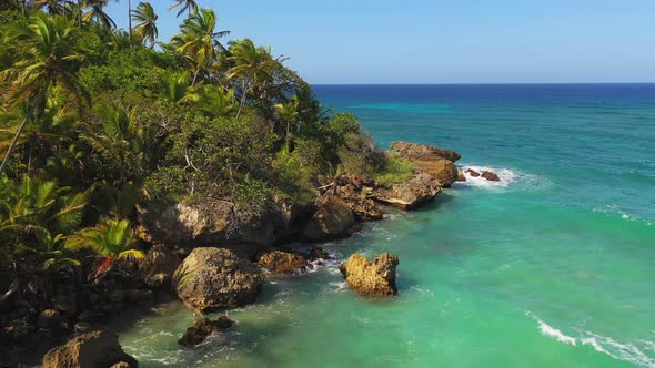 Spectacular low flight above rocky tropical remote coastline with green shallow water and waves brea alt