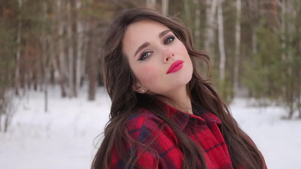 Young Woman with Wavy Hair Standing and Touching Face in Winter Forest