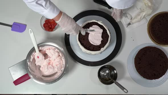 Overview of Chef Filling Up a Layer of Chocolate Cake with Pink Cream with the Help of Some Utensils alt