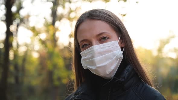 Woman in Medical Safety Protective Face Mask Walking Outdoors in Park