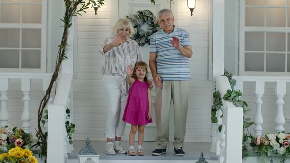Senior Grandparens Couple with Granddaughter in Porch at Home Waving Hand, Showing Thumbs Up alt