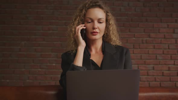 Businesswoman Having a Call on Her Phone While Working on a Laptop Computer alt