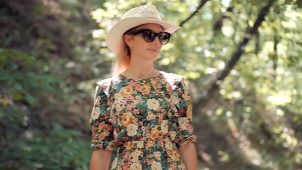 Woman In Hat Walking On Tree. Girl In Dress Walking In Greenwood. Female Exploring Green Forest. alt
